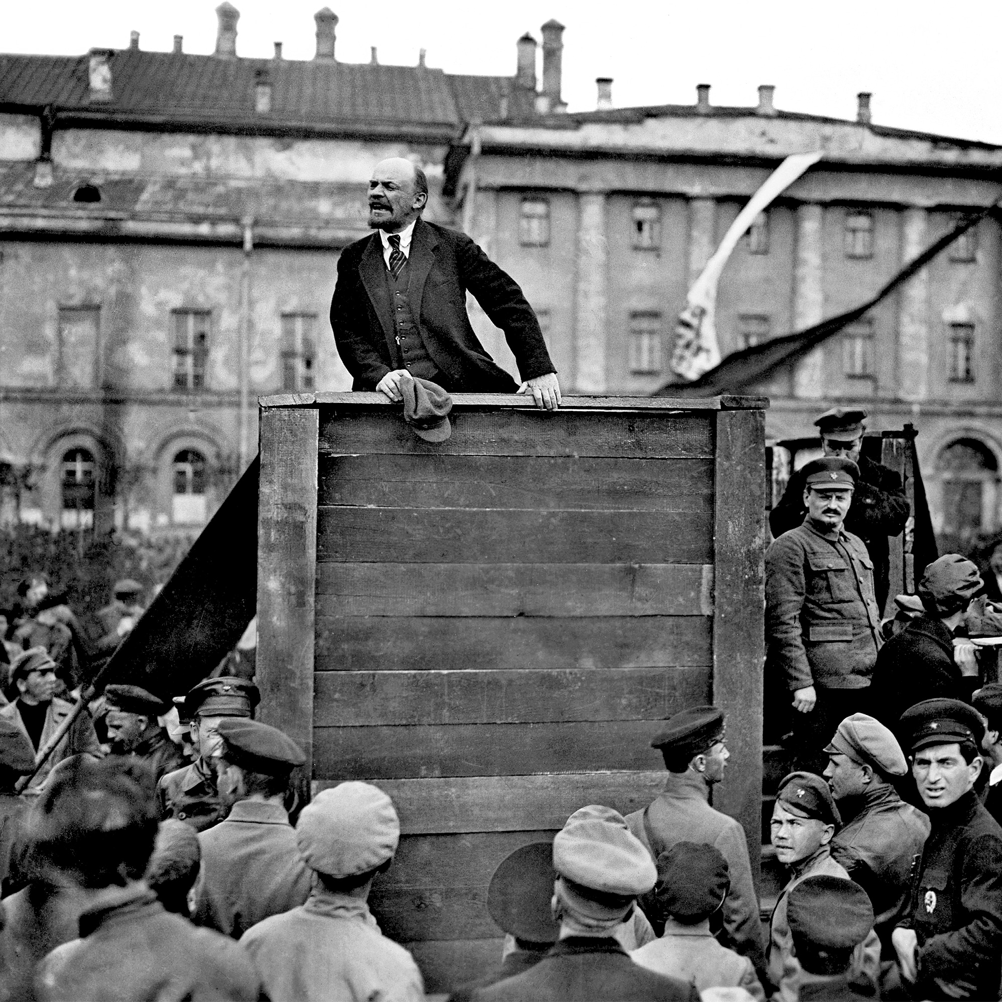 Lenin står i ett talarbås och agiterar till en omgivande folkmassa.