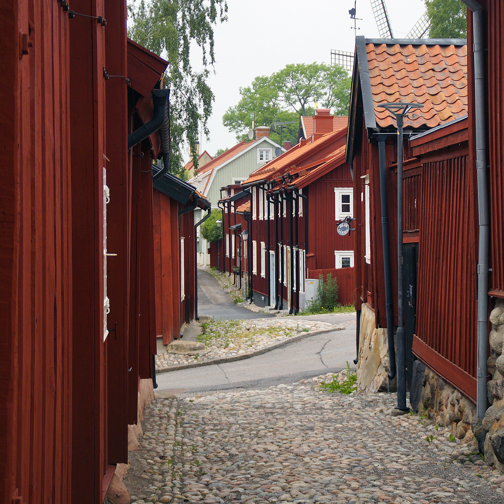 Gränd med kullersten. Gamla 1800-talshus i trä målade i falurött kantar den smala gatan.
