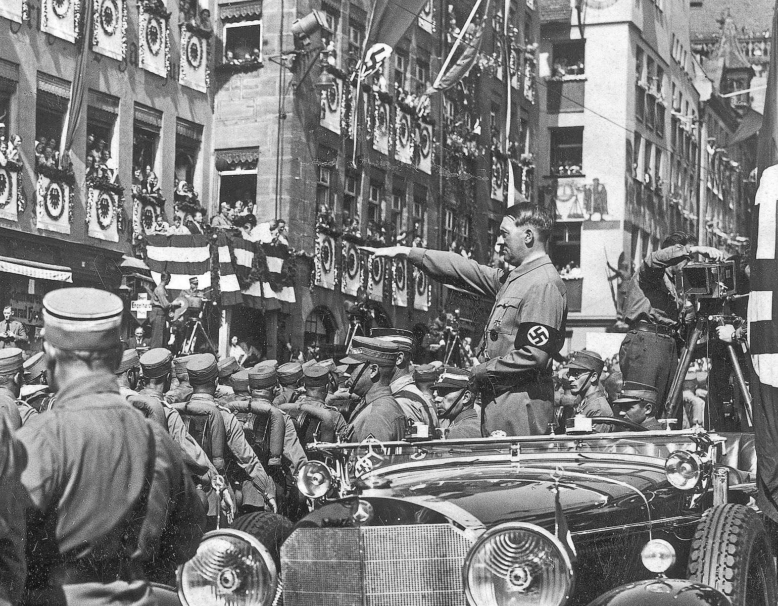 SA-trupper paraderar på en gata i Nürnberg 1934-. På bilden syns hitler ståendes i sin Merzedes och hälsar trupperna. Flera filmkameror syns i bild.