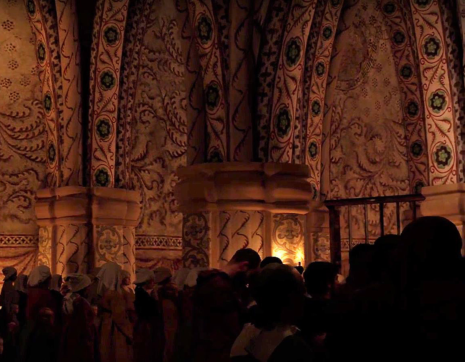 Interiör från kyrkan i Nya Lödöse. Församling på 1500-talet i skenet av stearinljus på väggarna.