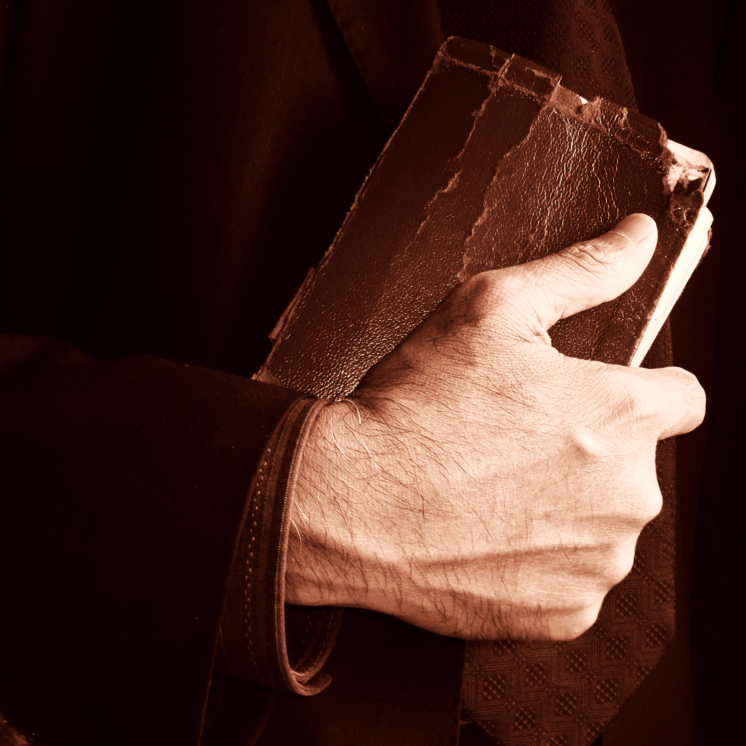 Svartkädd arm med hand som håller en gammal brun bibel.