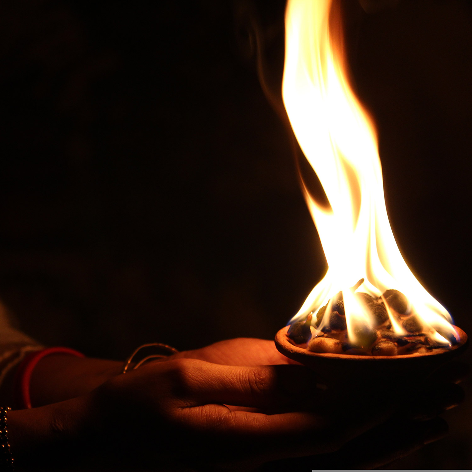Ett par händer som håller ett litet fyrfat med en flammande eld.
