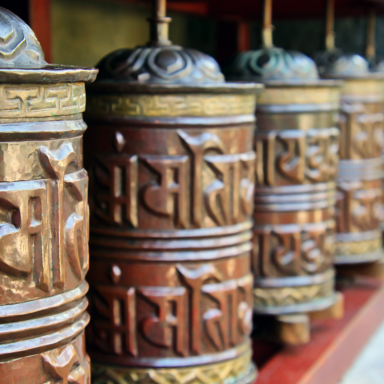 Stora bönehjul i mässing och koppar uppradade längs en gångväg.