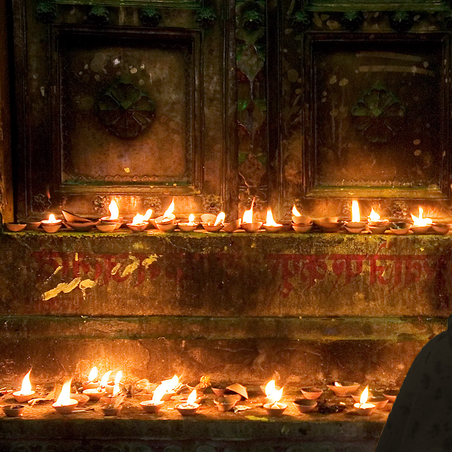 Många brinnande ljus på en trappa framför en dörr i ett tempel.