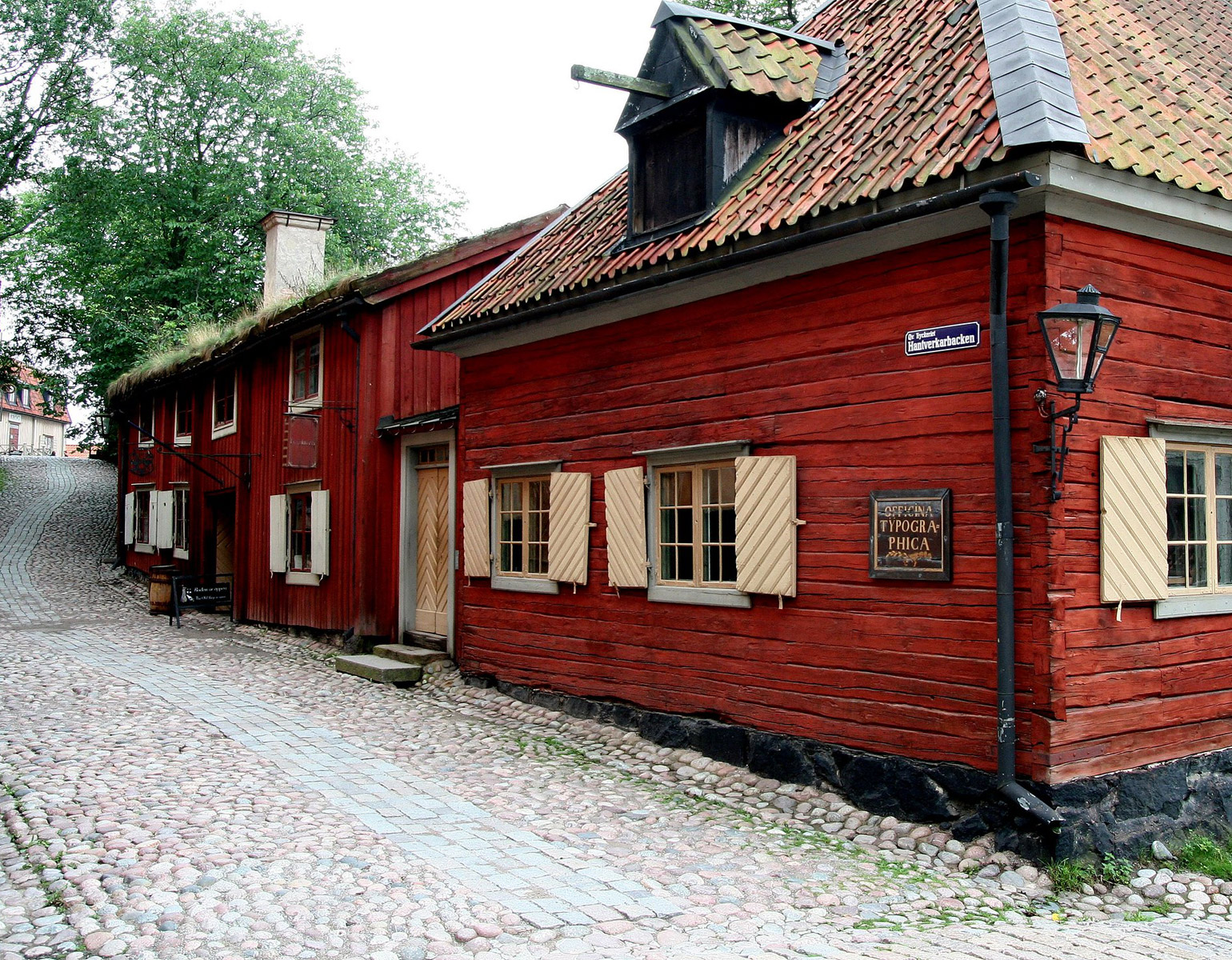 Gammalt rött trähus längs en kullerstensgata.