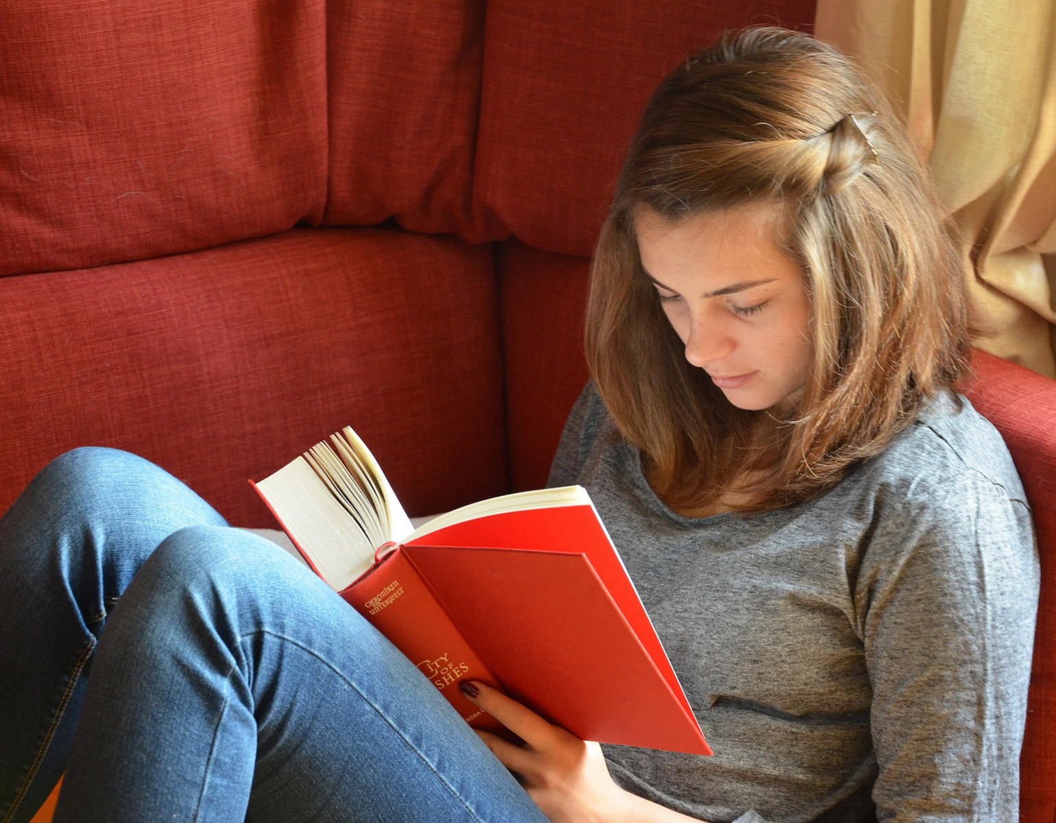 Tjej som läser en bok i en röd soffa.